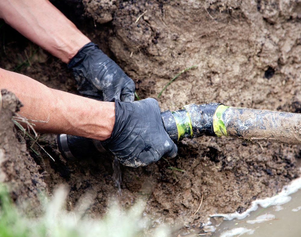 Hands working on outdoor pipes in the ground