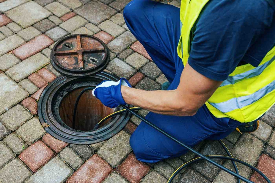 Plumber kneeling at a sewer cleanout with drain cables