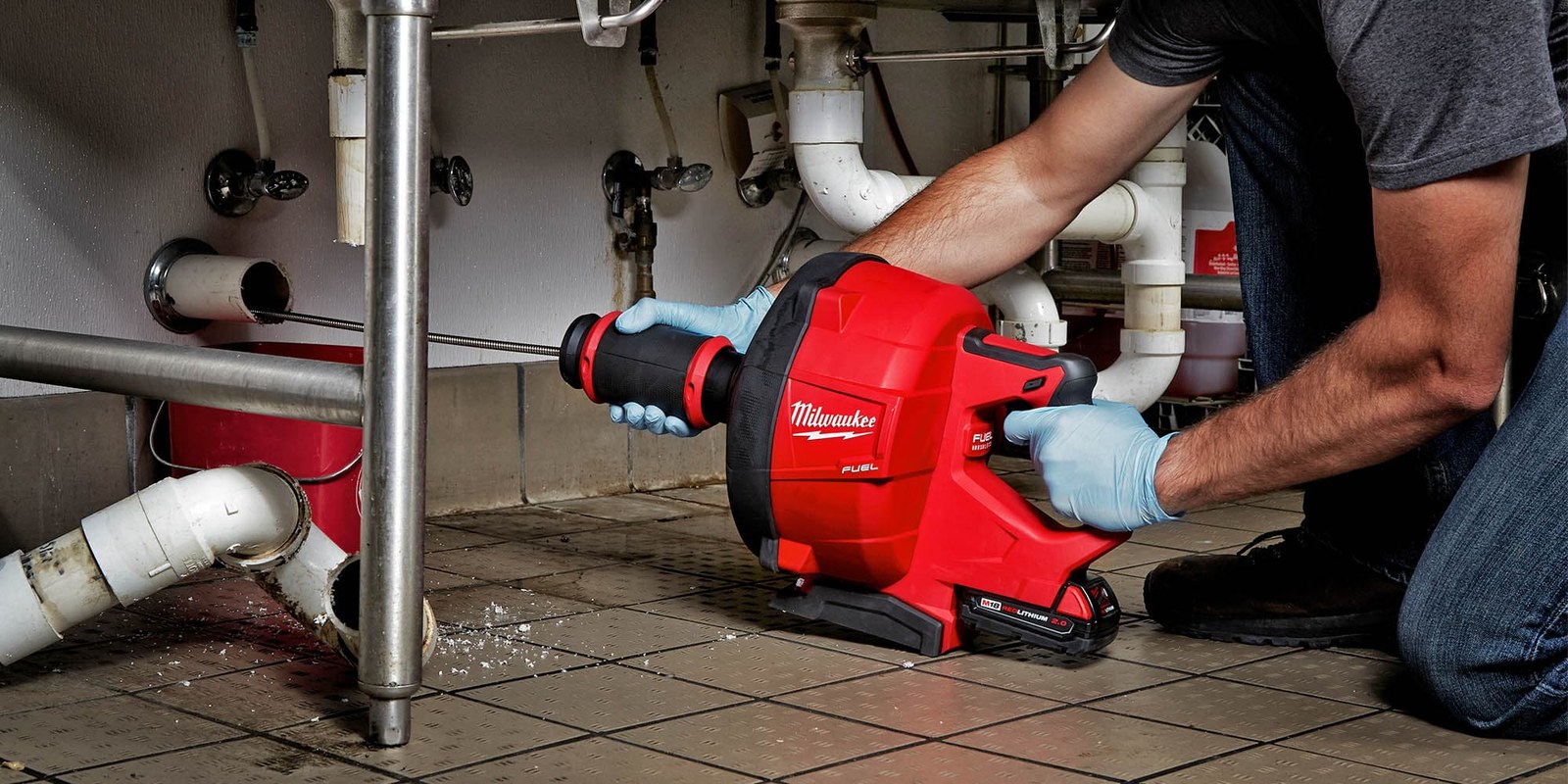 Plumber using a powered drain cleaning machine under a sink